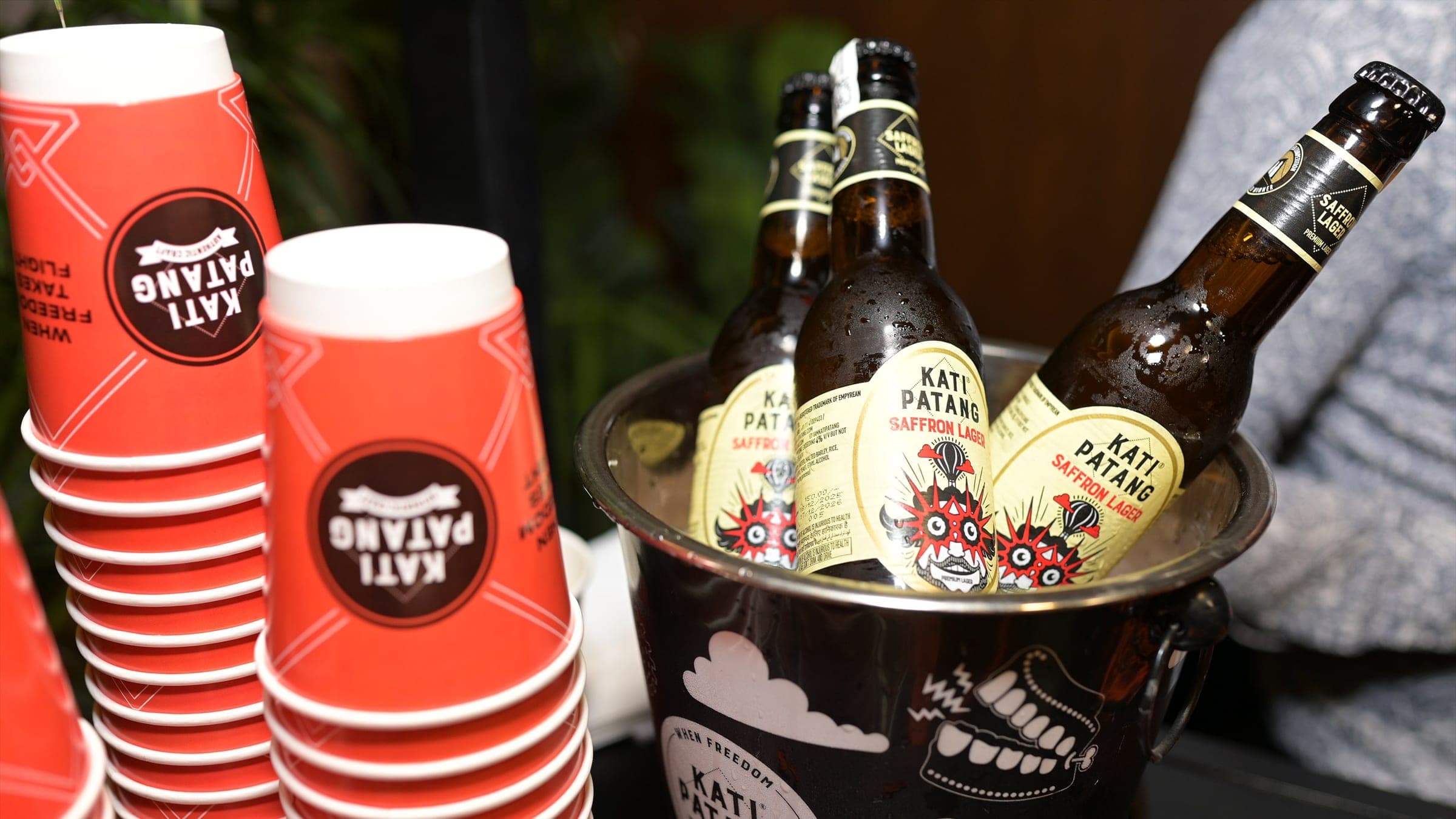 Bottles of Saffron Lager on ice beside a stack of Kati Patang cups