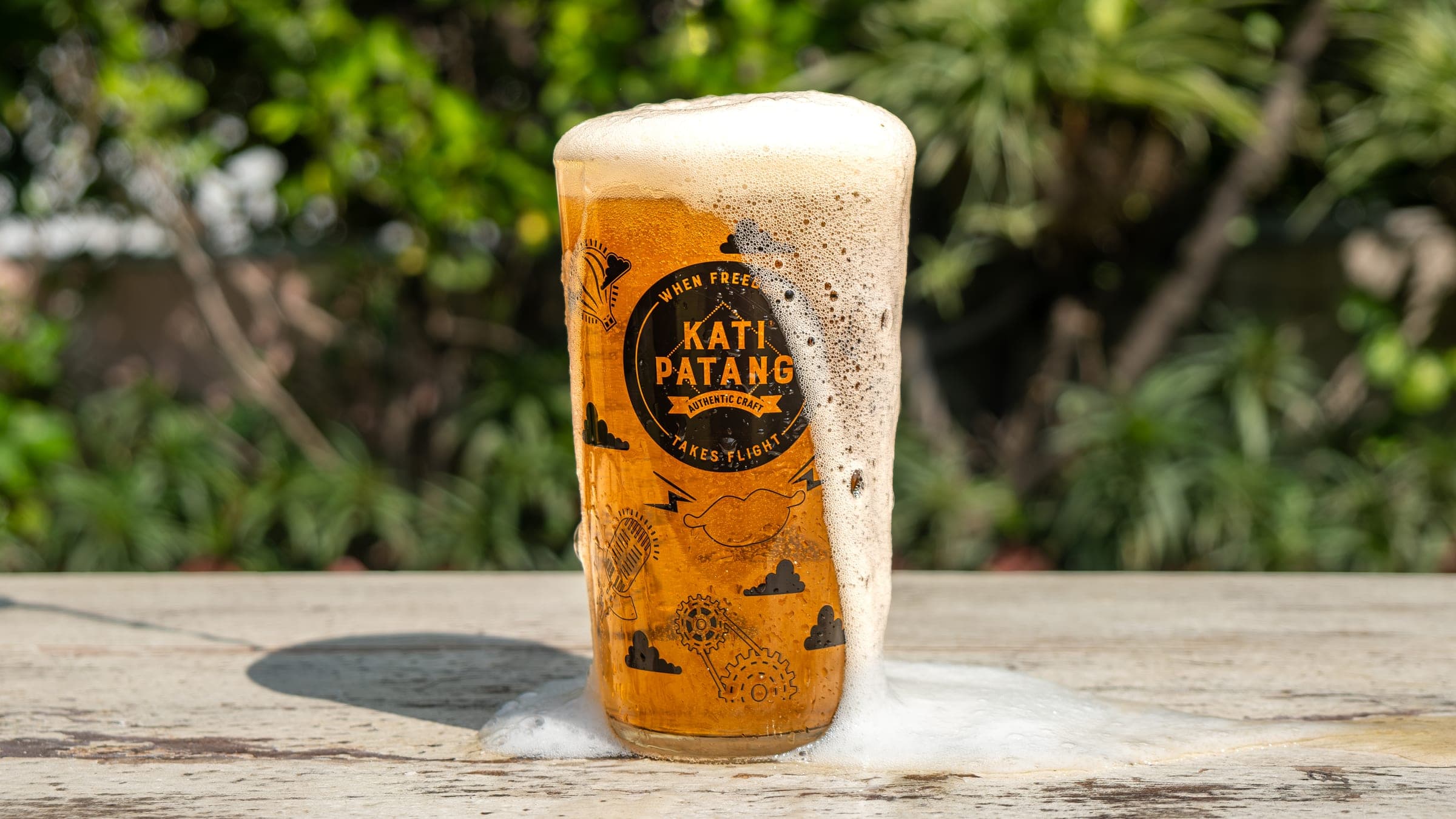 A branded Kati Patang pint glass filled with beer, foam spilling over the rim