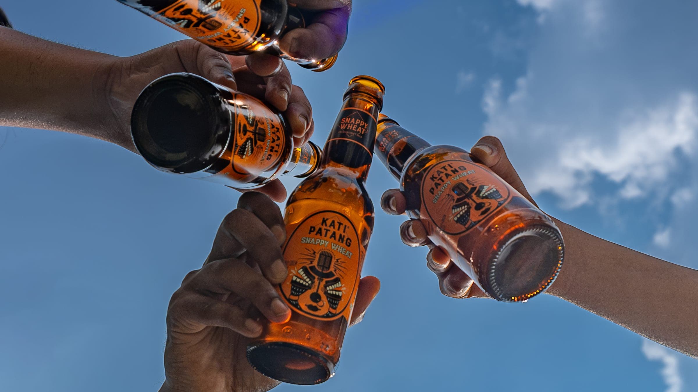Four bottles of Kati Patang Snappy Wheat raised against an open sky